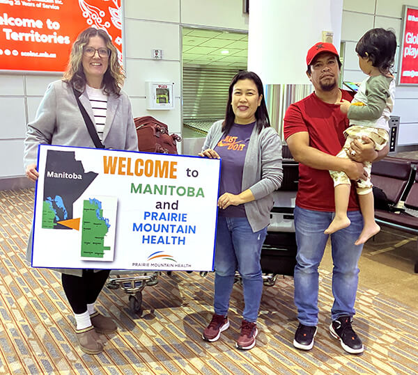 Larissa, Mae, Garry & son holding welcome sign at Winnipeg airport.