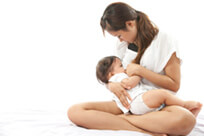 Image of a woman sitting cross legged breast feeding her baby.