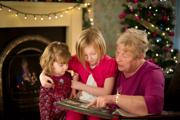 Woman and granddaughters looking at photos by Christmas tree.