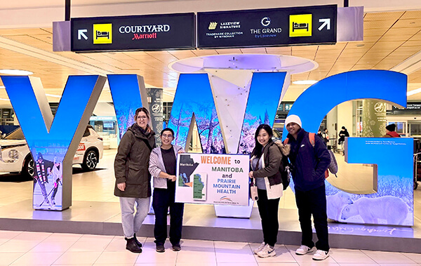 Larissa, Jackline, Felica & Carlo holding welcome sign at winnipeg airport
