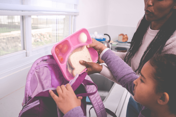 Mother and daughter packing lunch box into the kid backpack.